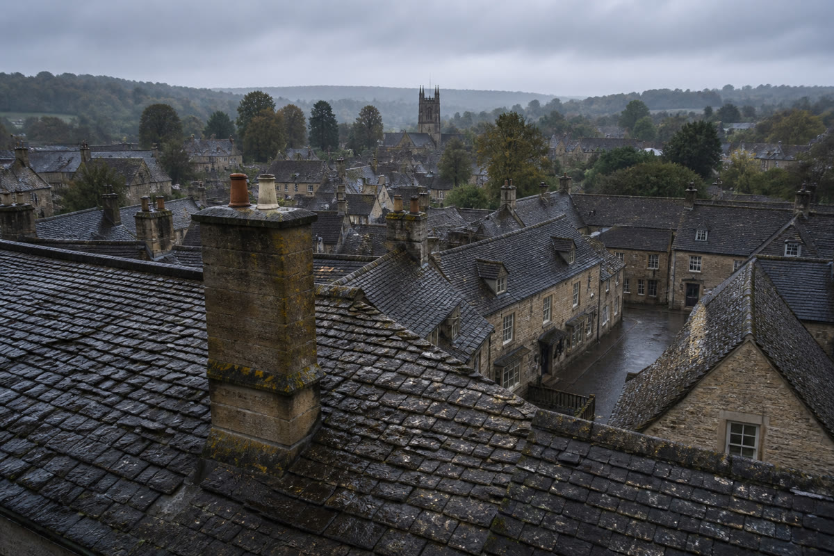 Wet slate rooftops and chimney pots of a Cotswold market town under a pewter sky